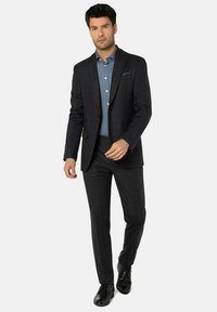 Dunkler Herrenanzug mit Muster, bestehend aus einem maßgeschneiderten Sakko und eng anliegenden Hosen, kombiniert mit einem hellblauen Hemd und schwarzen Anzugschuhen.