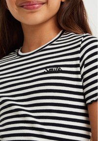 Camiseta de rayas blancas y negras con textura acanalada, presenta un cuello redondo, mangas cortas y un detalle bordado de "Sonrisa" en el pecho.