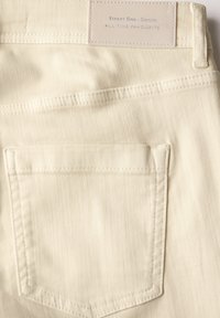 Tela de mezclilla beige con una textura suave, que presenta un bolsillo trasero y una etiqueta que dice "Street One - Denim" cosida en la parte superior.