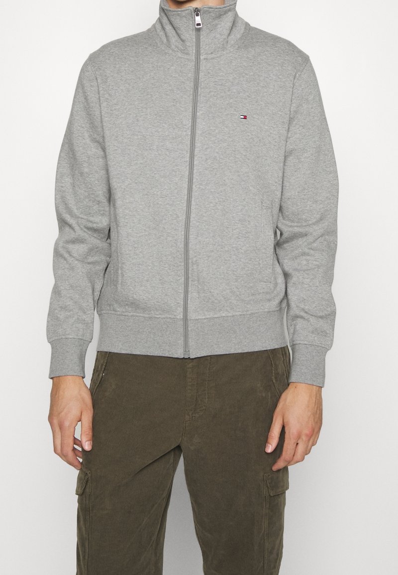 Gray zip-up sweatshirt with a high collar, made of soft fabric, featuring a small logo on the left chest and ribbed cuffs and hem.