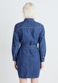 Denim shirt dress in dark blue, featuring long sleeves, button cuffs, a belted waist, and a straight silhouette. Seams visible along the back.