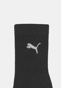 Chaussette noire à cotes avec un logo Puma blanc sur le côté. Le bord est replié, mettant en avant la texture et le matériau.