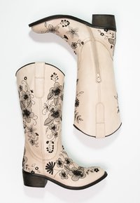 Stivali alti in pelle crema con ricami floreali neri, chiusura con zip e tacco in legno impilato. Texture liscia e design a punta.