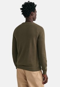 Olijfgroene gebreide trui met een gestructureerd patroon, ribbelmanchetten en elastische tailleband. Beschikt over een klassiek ronde halsontwerp en heeft een ontspannen pasvorm.
