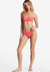 Rosa bikini set med en texturerad tyg, inkluderande en bralette topp och matchande lågt skurna underdelar. Justerbara band och minimal täckning.