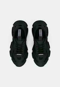 Sorte atletiksko med mesh- og gummimaterialer, snøredesign, rundet tå og teksturerede detaljer for greb og støtte.