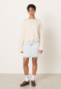 Krémový, nadýchaný pletený svetr s výstřihem do V, doplněný světle modrou džínovou sukní. Hnědé boty se šněrováním a bílé ponožky s nápisy.