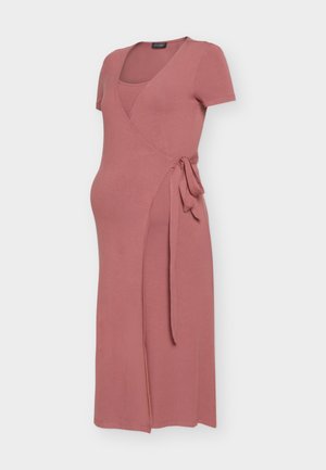 Staubrosafarbener knielanger Umstands-Wickelkleid mit kurzen Ärmeln und seitlicher Bindung vor einfarbigem Hintergrund.