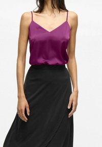 Camisole violet en satin avec un décolleté en V et des fines bretelles, associé à une jupe portefeuille noire. Texture lisse avec une légère brillance.