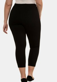 Mustat, venyvät legginsit elastisella vyötäröllä. Keskivartalon pituinen, sileä pinta, suunniteltu mukavuutta ja liikkuvuutta varten.