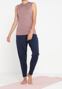 Haut de sport sans manches mauve clair associé à un pantalon tapered bleu marine foncé ; tissu lisse, coupe décontractée, sans motifs ni accessoires visibles.