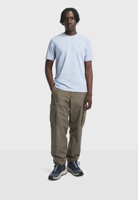 T-shirt in cotone azzurro chiaro con colletto a girocollo, abbinato a pantaloni cargo khaki con tasche laterali e scarpe sportive blu scuro e nere.