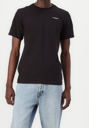 T-shirt noir à manches courtes avec petit logo blanc "G-STAR RAW" sur la poitrine gauche, porté avec un jean denim bleu clair.