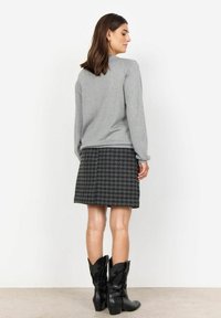 Harmaa pitkähihainen paita yhdistettynä polvimittaisiin mustavalkoisiin houndstooth-huusuihin ja mustiin cowboy-korkokenkiin, joissa on monimutkaiset ompeleet.