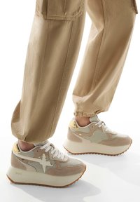 Sneaker beige e crema realizzati in materiali mesh e suede, con texture contrastanti, suole bianche spesse e dettagli dorati sul tallone.