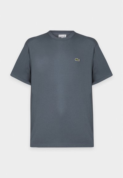 T-shirt gris foncé à manches courtes et col rond avec un petit logo crocodile vert sur la poitrine gauche, présenté sur un fond clair uni.
