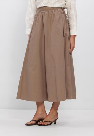 Bruine midi-rok met zijstrik in de taille, gedragen met een witte blouse en bruine sandalen met lage hak op een lichte achtergrond.