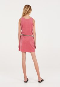 Abito in terry cloth rosa con vestibilità ampia, design senza maniche e vita elastica. Orlo piatto abbinato a sandali neri.