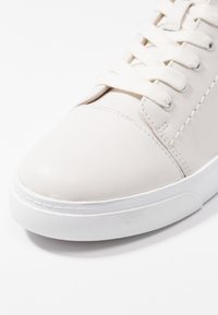 Valkoiset nahkakenkä, jossa on sileä pinta, pyöreä kärki ja sävyyn sopivat nauhat. Sisältää ompeluyksityiskohtia ja valkoisen kumipohjan.