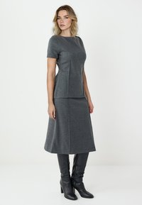 Graues gestricktes Zweiteiler-Outfit mit einem kurzärmeligen Oberteil und einem ausgestellten Rock, kombiniert mit schwarzen knielangen Heels-Stiefeln. Glatte Textur.