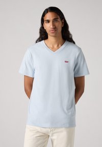 Lyseblå V-hals t-skjorte laget av myk bomull, med korte ermer og en liten rød Levi's-logo på venstre bryst. Enkel design.