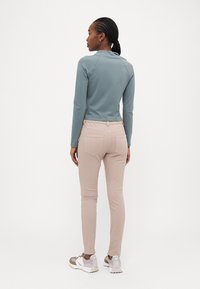 Top de manga larga azul claro, diseño ajustado, combinado con jeans ajustados beige claros. Zapatillas blancas y grises con suelas texturizadas. Líneas simples y limpias.