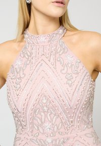 Abito rosa con scollo halter decorato con intricati gioielli di perline e perle, caratterizzato da un motivo a zigzag e accenti floreali. Texture in seta liscia.