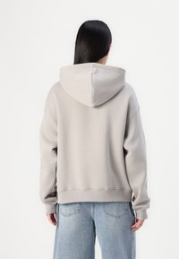 Hoodie gris clair à la coupe ample, avec une capuche à cordon et des poignets côtelés. Assorti à un pantalon en denim bleu ample.