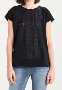 Mustat puuvillapaidat, joissa on lyhyet hihat, ja keskellä on monimutkainen leikkauskuvio. Yhdistettynä vaaleansinisiin farkkuihin.