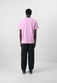 Rosa bomullströja med korta ärmar, kombinerad med svarta fluffiga byxor. Skorna är mörka sneakers. Enkel och funktionell design.