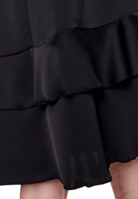 Vestido negro con diseño de volantes en capas, textura de tela suave y detalles en el dobladillo; acabado suave con costuras visibles a lo largo de los bordes.