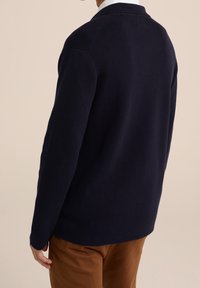 Tmavě námořnický pletený kardigan se strukturovaným límcem, dlouhými rukávy a volným střihem, vyrobený z měkké texturované látky.