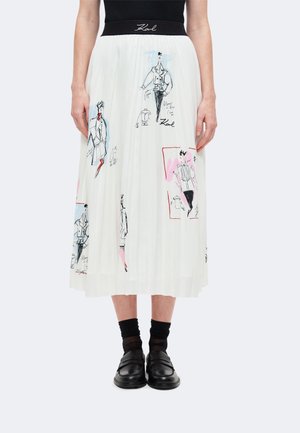 Jupe midi plissée blanche avec taille noire et croquis de mode abstraits et colorés, portée avec des mocassins noirs et des chaussettes noires transparentes.