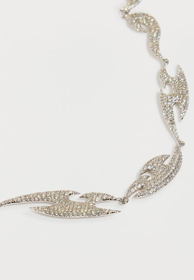 Srebrna ogrlica z združenimi segmenti v obliki plamenov, okrašenimi z majhnimi prozornimi kristalčki, ki prikazujejo sijoč kovinski zaključek in zapleten dizajn.