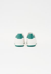 Hvite sneakers med en teksturert teal accenter på hælen. Gummisåle med mønstret grep. Minimalistisk design, snøring.