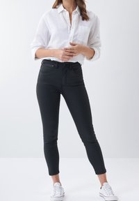 Black skinny jeans with a high waist, featuring front pockets and belt loops. Paired with a white button-up shirt. Worn with white sneakers.