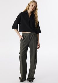 Czarna krótka koszulka polo z kołnierzykiem i kieszonką z przodu, sparowana z oliwkowo-zielonymi spodniami cargo w szerszym kroju, które mają boczne kieszenie i płaski przód.