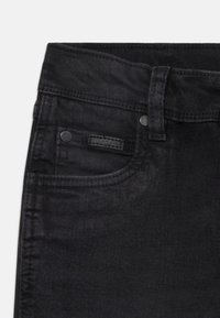 Svarta denimjeans med en slät yta, som har en framficka, en liten logotyp på fickan och metallnitar.