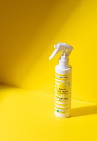 Spruzzatore bianco con erogatore a pistola. Design a strisce gialle e bianche. Etichetta recante la scritta "Balsamo spray bifasico" con loghi ecologici.