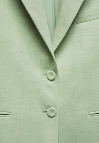 Light green blazer with a textured fabric, two round buttons, and two front pockets. Features a notched collar and tailored fit.