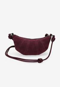 Bolso de ante burdeos con un diseño redondeado, que presenta un cierre de cremallera, asas laterales anudadas y detalles de paneles cosidos visibles.