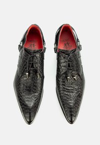 Schwarze Lederschuhe mit Krokodillederoptik, spitzem Zeh, Schnürdesign und rotem Innenfutter. Silberfarbene Hardware-Akzente sind vorhanden.