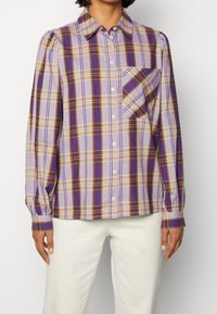 Purple plaid shirt with long sleeves, a button-up front, and a single chest pocket. Features light and dark stripes in yellow and brown.