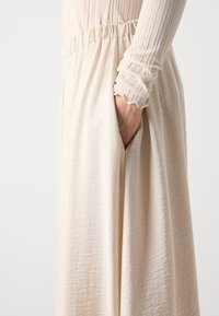 Flared, cream-colored skirt with a soft, textured fabric. Features an elastic waistband and a side pocket, emphasizing relaxed styling.