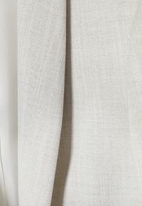 Gros plan sur un tissu tissé beige clair avec une texture légèrement rugueuse et un motif discret de tissage diagonal.