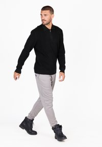 Schwarzes Polo mit langen Ärmeln und Reißverschlusskragen, kombiniert mit hellgrauen Jogginghosen und schwarzen Schnürstiefeln. Einfaches Design und lässige Passform.