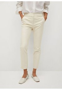 Pantaloni cream su misura con tasche laterali, slim fit, realizzati in tessuto morbido. Abbinati a scarpe leggere e basse con dettagli arricciati.