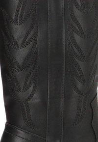 Bota de cuero negro con un intrincado bordado en un patrón de hojas a lo largo del eje. Textura suave con un diseño ajustado.