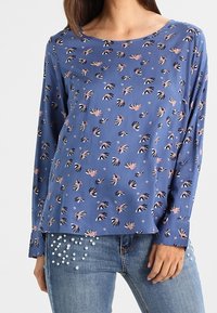 Maglietta blu a maniche lunghe con motivi floreali in rosa e nero, scollo rotondo e vestibilità comoda, abbinata a jeans con dettagli in perle.