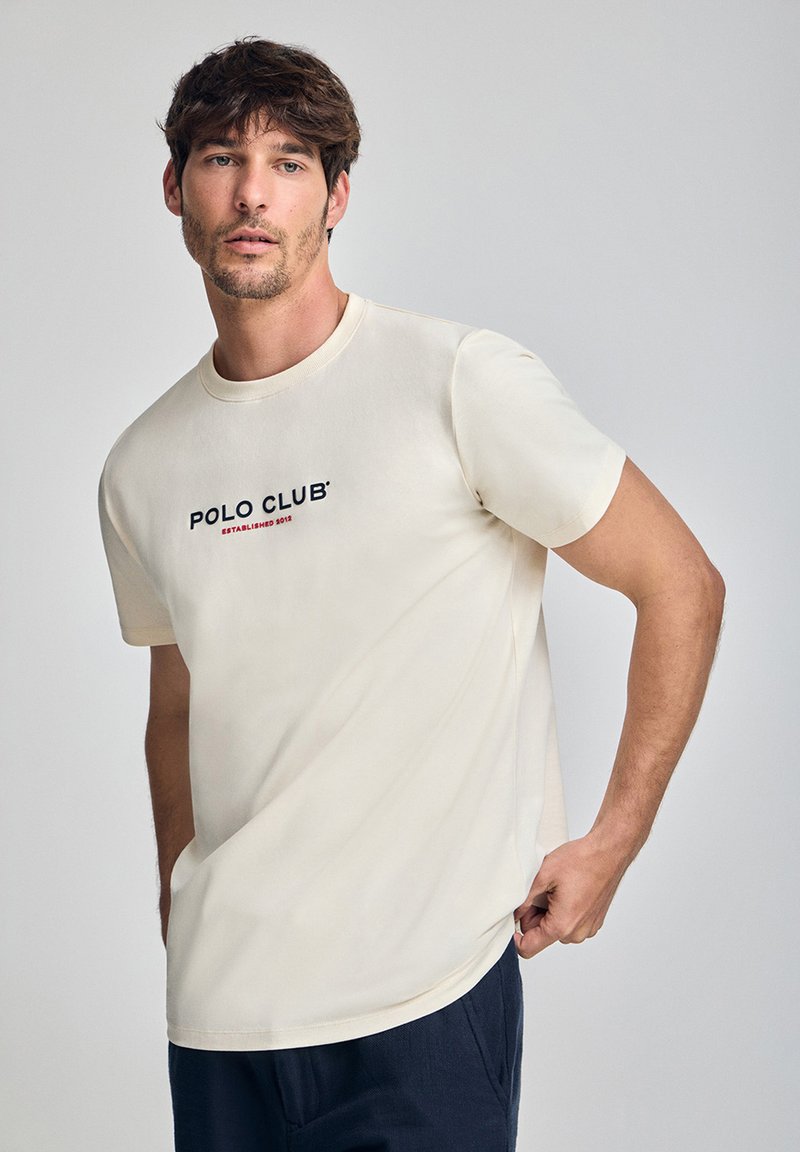 Kremowa bawełniana koszulka z krótkim rękawem, z logo "POLO CLUB" oraz rokiem założenia nadrukowanym w granatowym i czerwonym na przodzie.